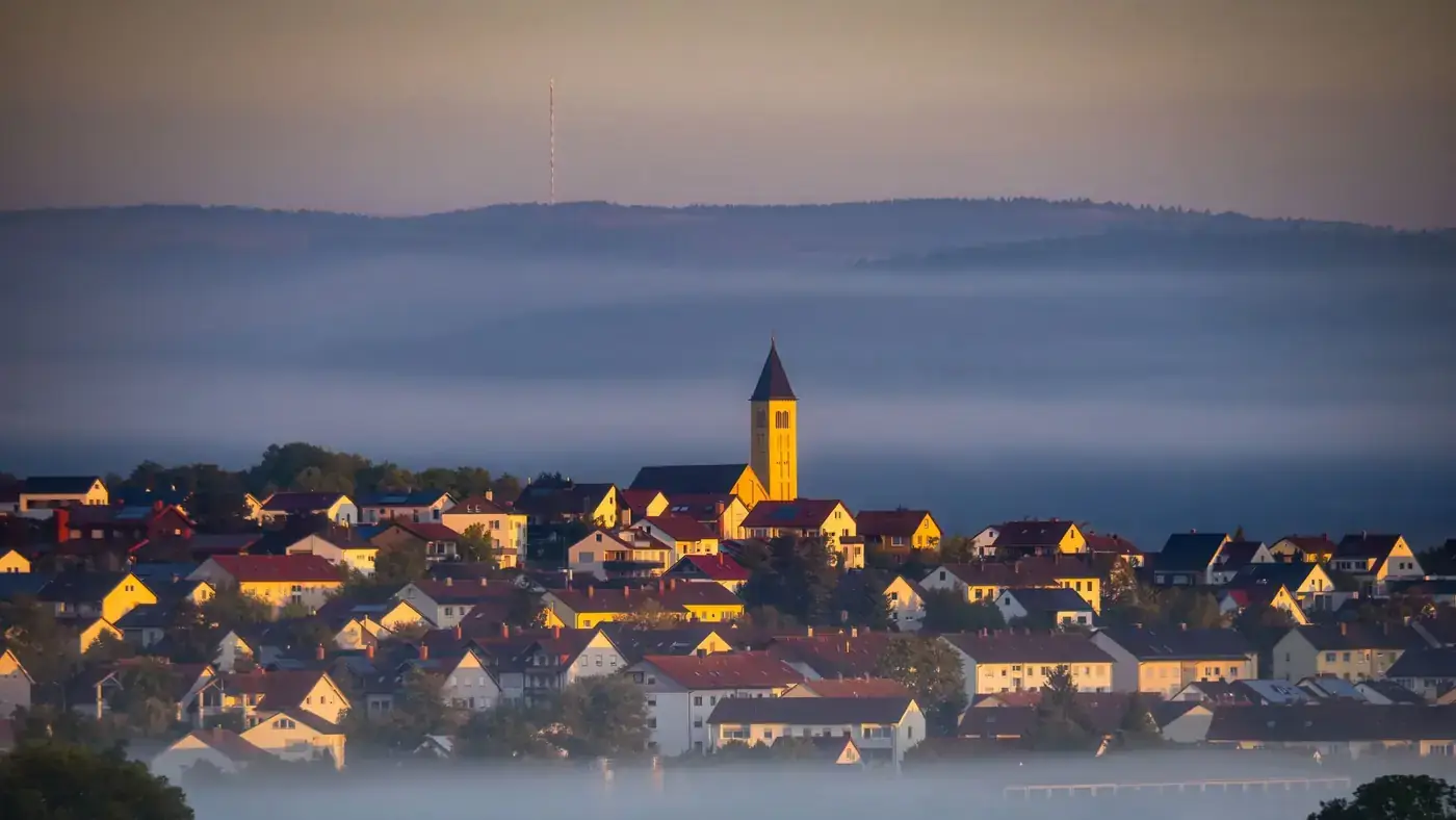 Captivating view of Bad Neustadt, Germany at sunrise, enveloped in mist and warm light.