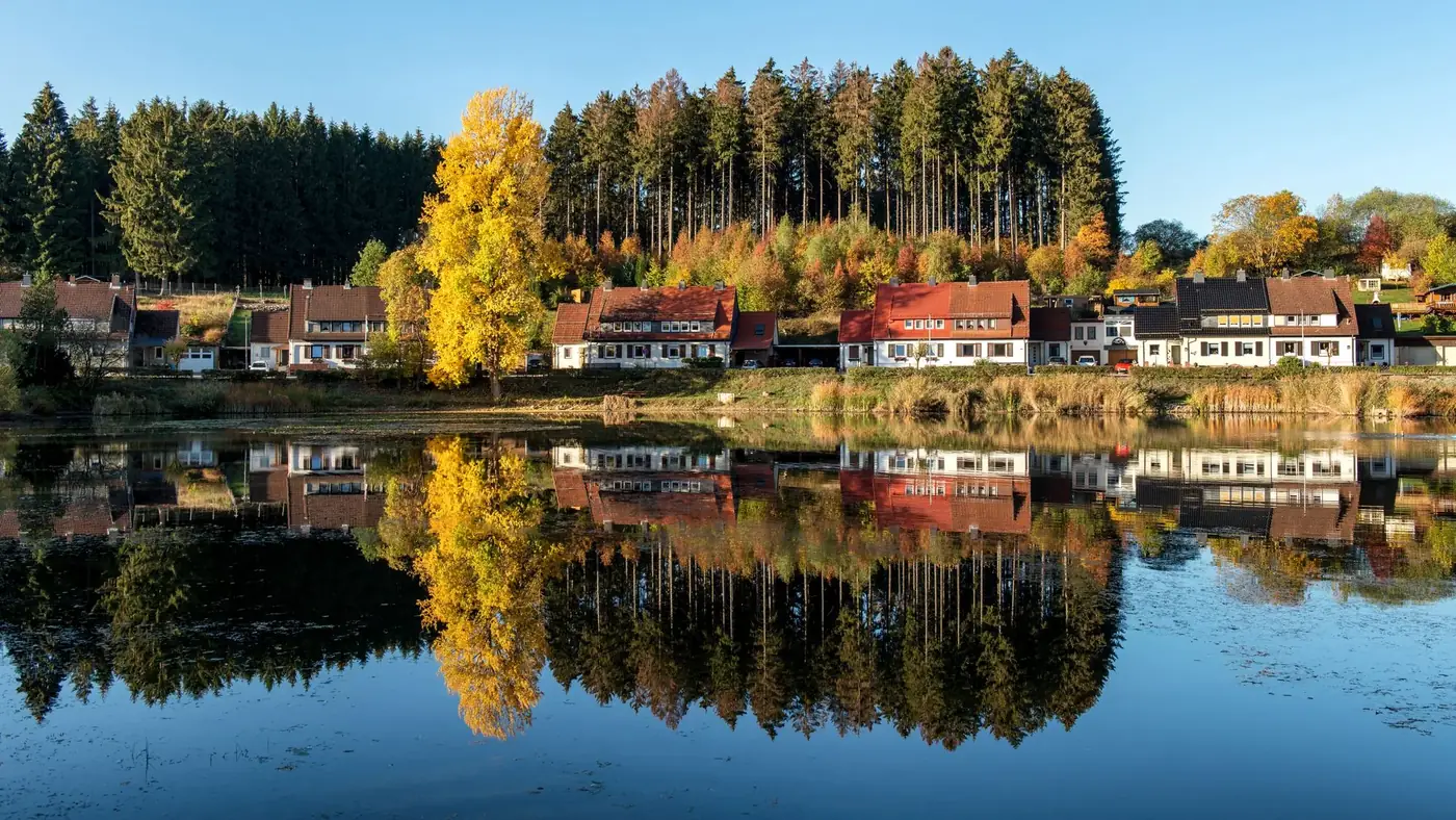 Charming village houses reflecting in a serene lake surrounded by autumn foliage in Bad Grund, Germany.