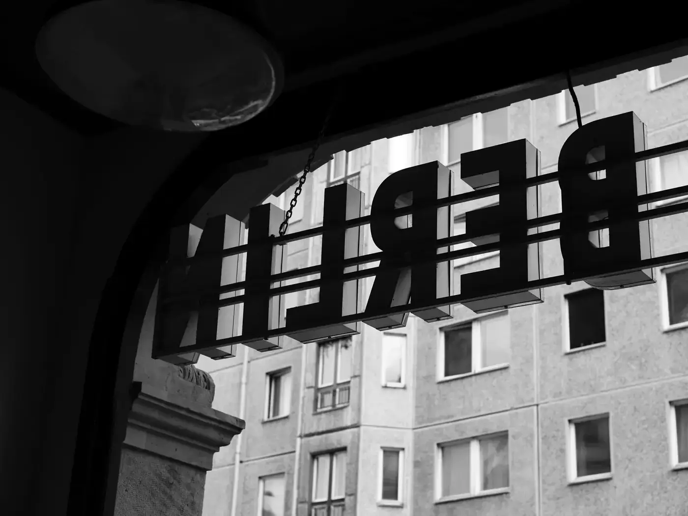 Black and white reflection of a 'BERLIN' sign with urban architecture in the background.