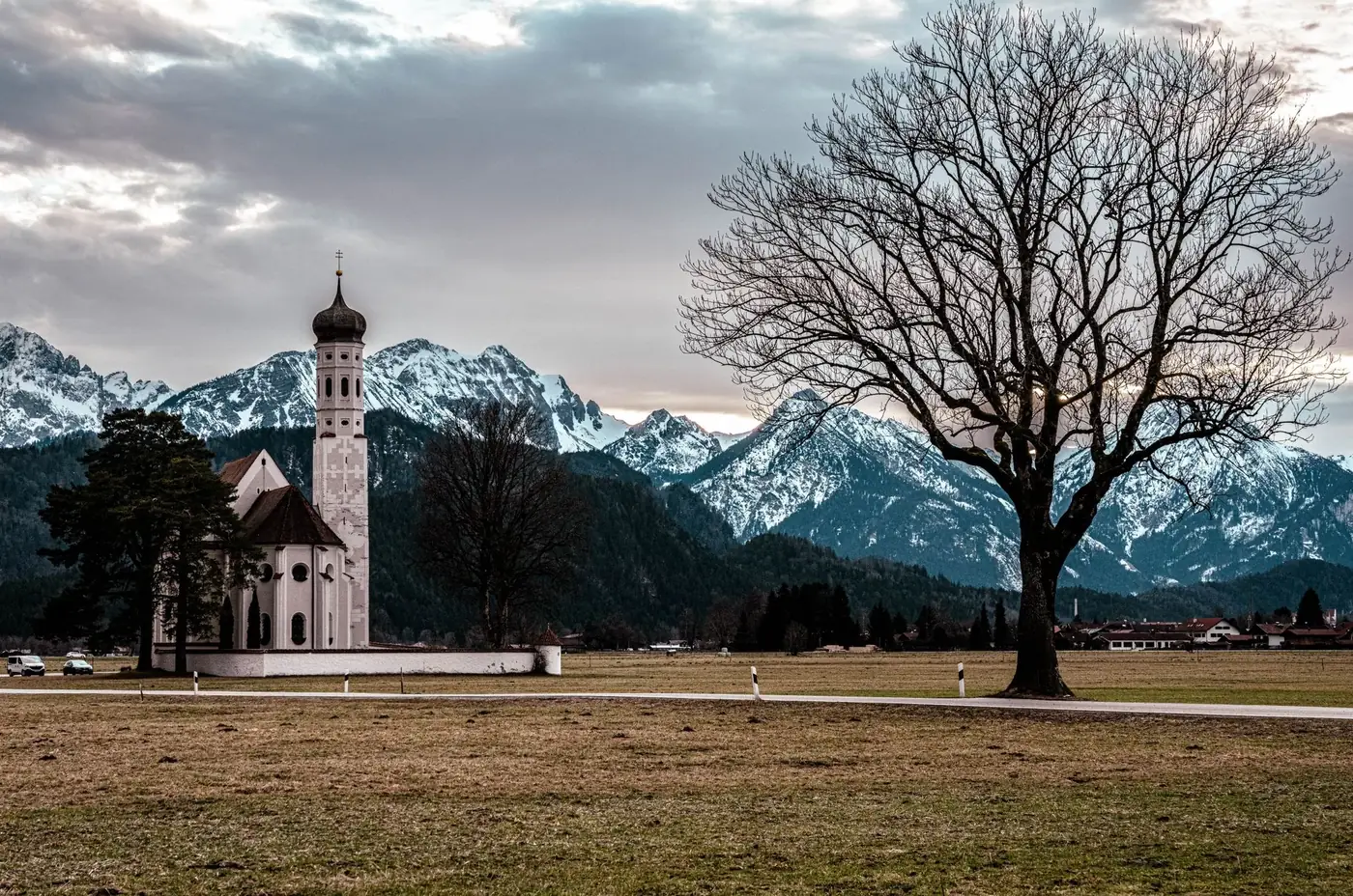 St. Coloman Church near snowy Bavarian Alps in Schwangau, Germany, under a cloudy sky.