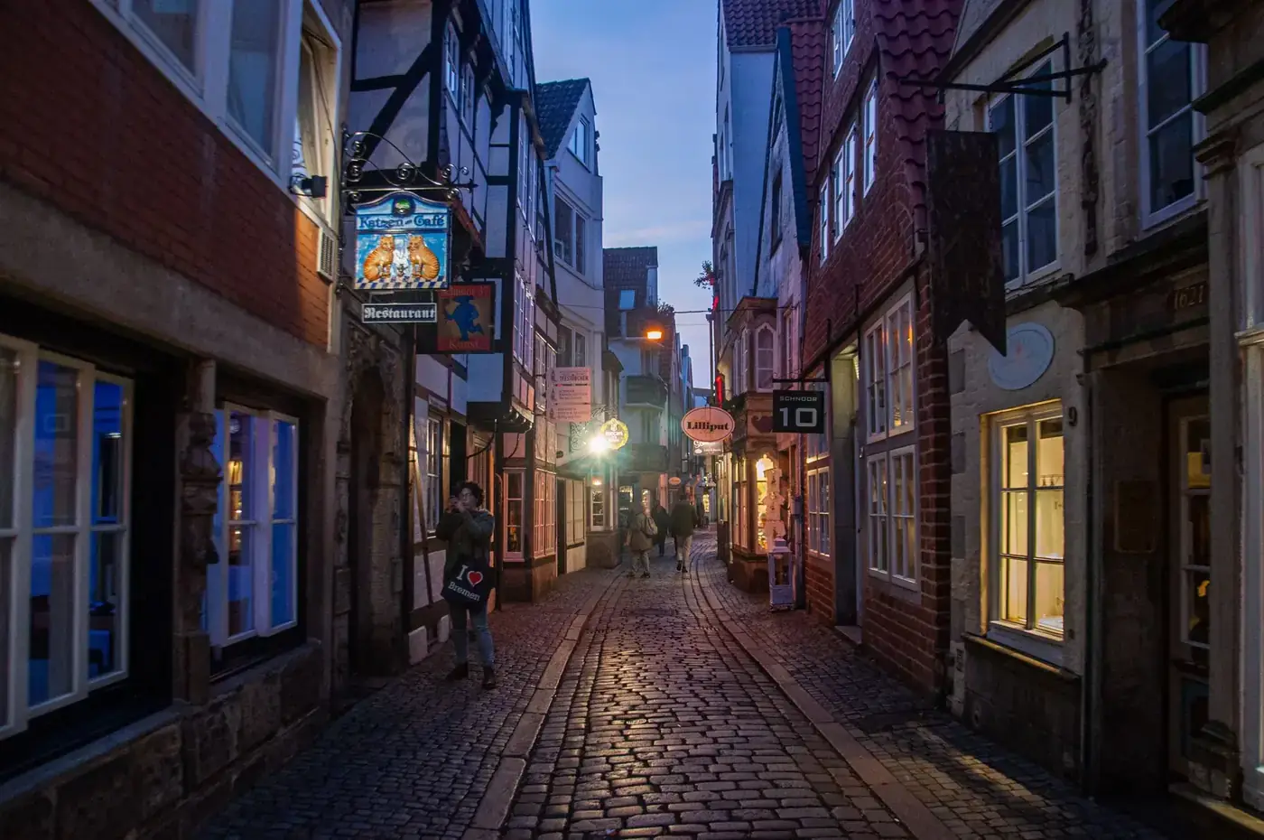 A quaint European alley with lit storefronts and cobblestones at twilight, capturing a warm atmosphere.