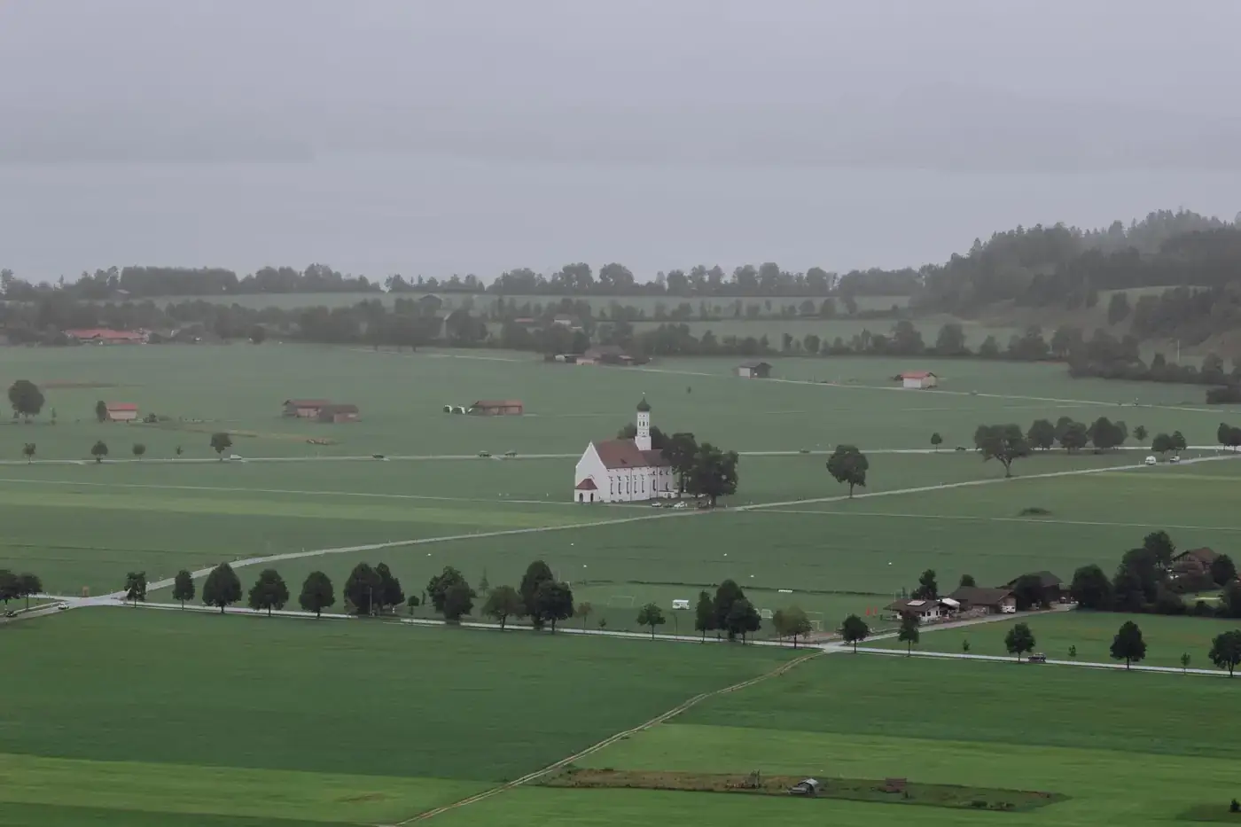 Aerial view of a picturesque Bavarian village with a central chapel surrounded by lush green fields.