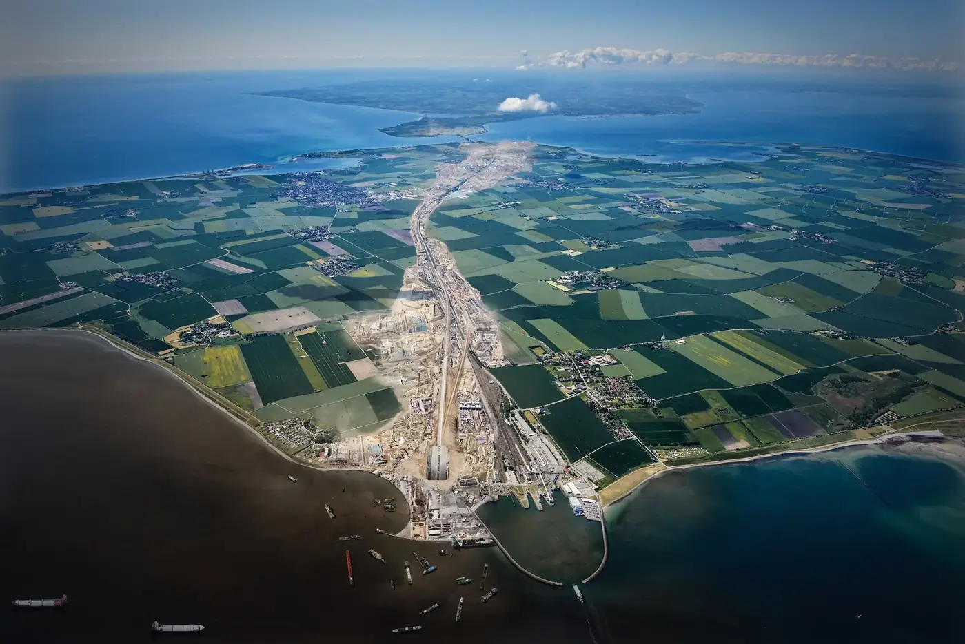 Aerial view of construction site and landscape on Fehmarn, Germany with ocean and ships.