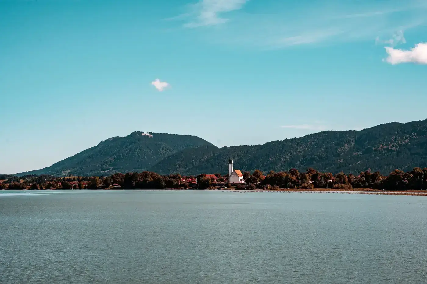 Picturesque landscape of a serene lake with mountains in the background under a blue sky.