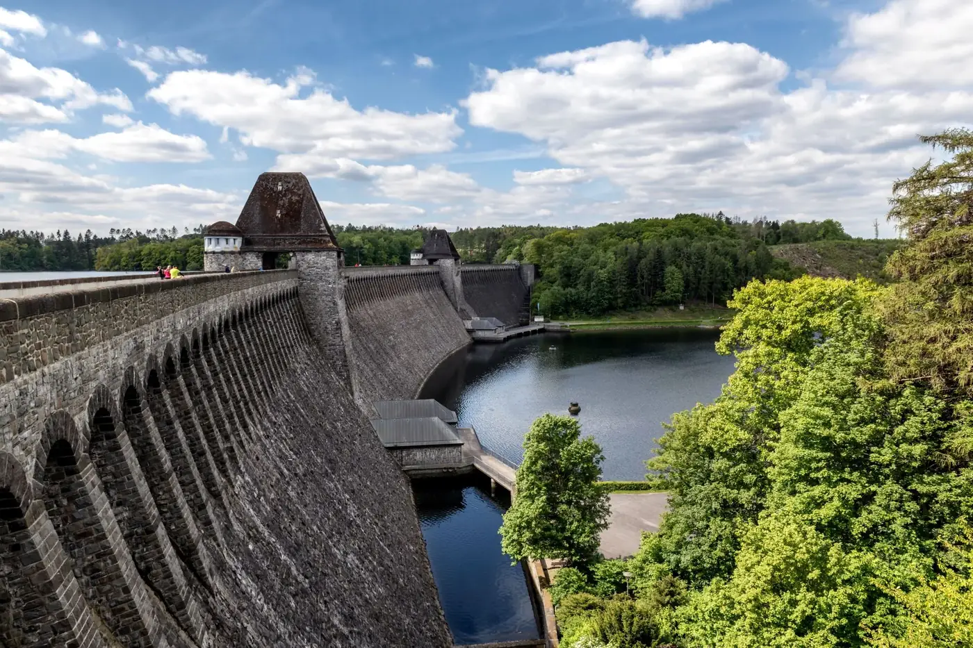 Dramatic view of the Möhne Reservoir dam surrounded by lush forests and clear skies.