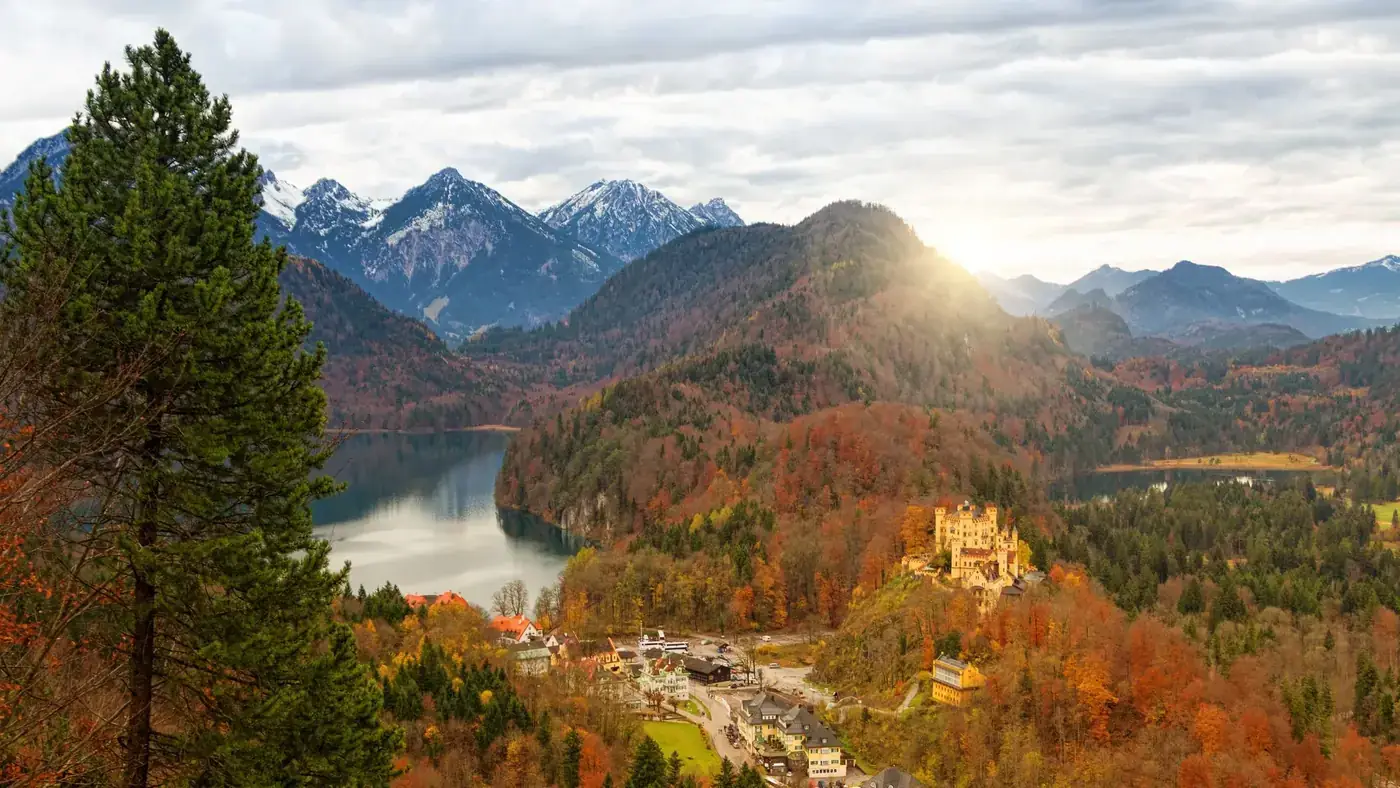 Stunning autumn view of Hohenschwangau Castle amid mountains, lake, and forest.