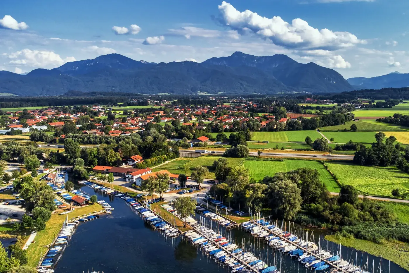 Vibrant aerial view of a marina and small town nestled against a majestic mountain range under a bright blue sky.