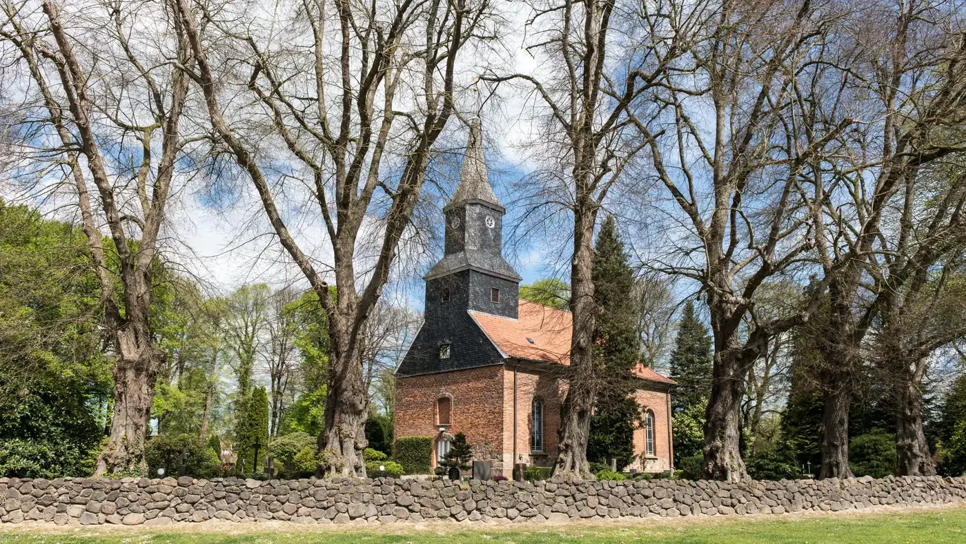 Scenic view of a historic brick chapel in Brunstorf, surrounded by trees and stone wall.