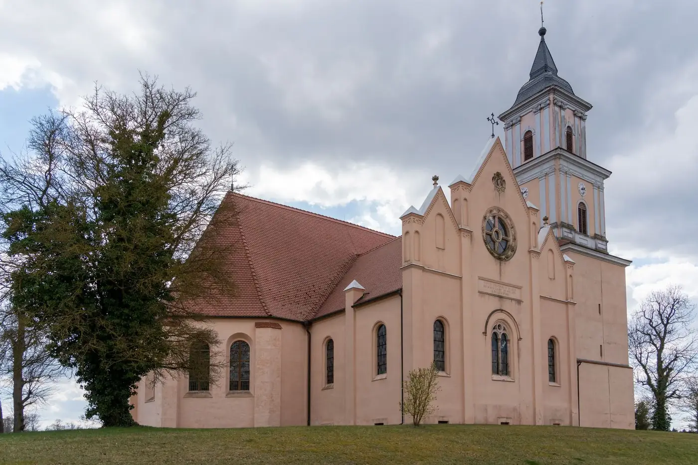 A picturesque historic church with a steeple, set against a serene rural backdrop and cloudy sky.
