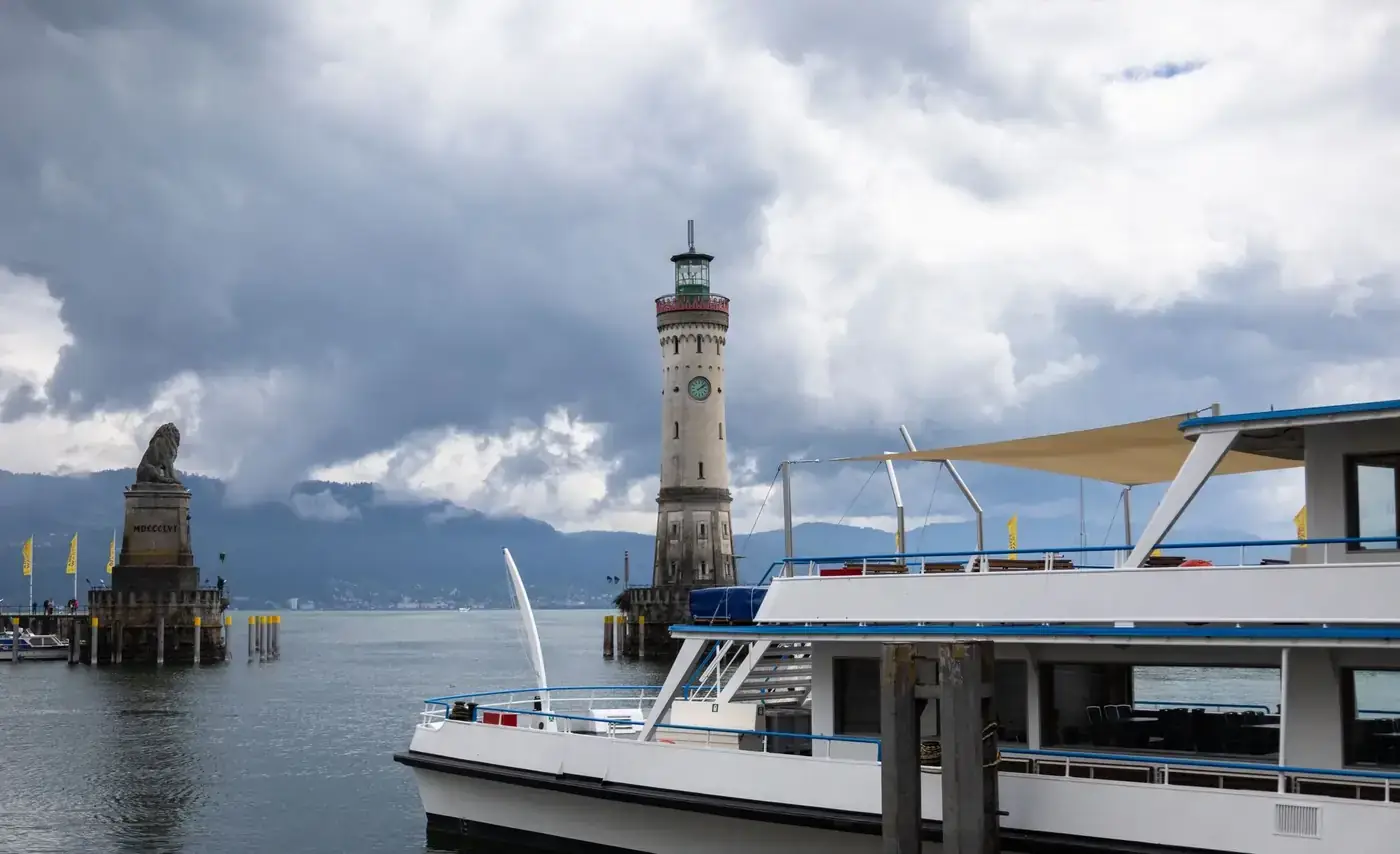 View of Lindau Lighthouse and a boat at Lake Constance under cloudy skies.
