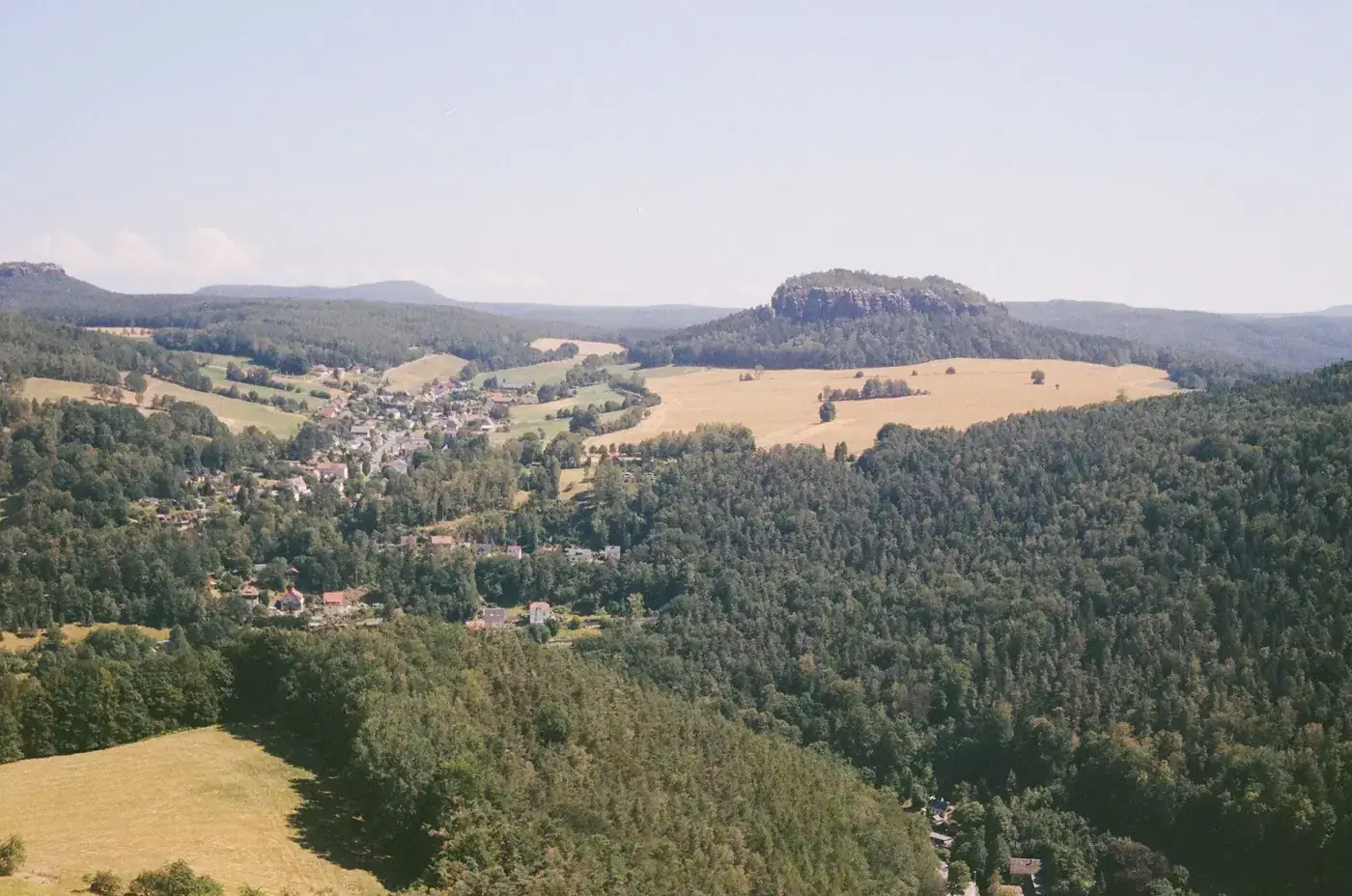 Aerial view of Königstein, Saxony, showcasing lush forests and rolling hills under a clear sky.