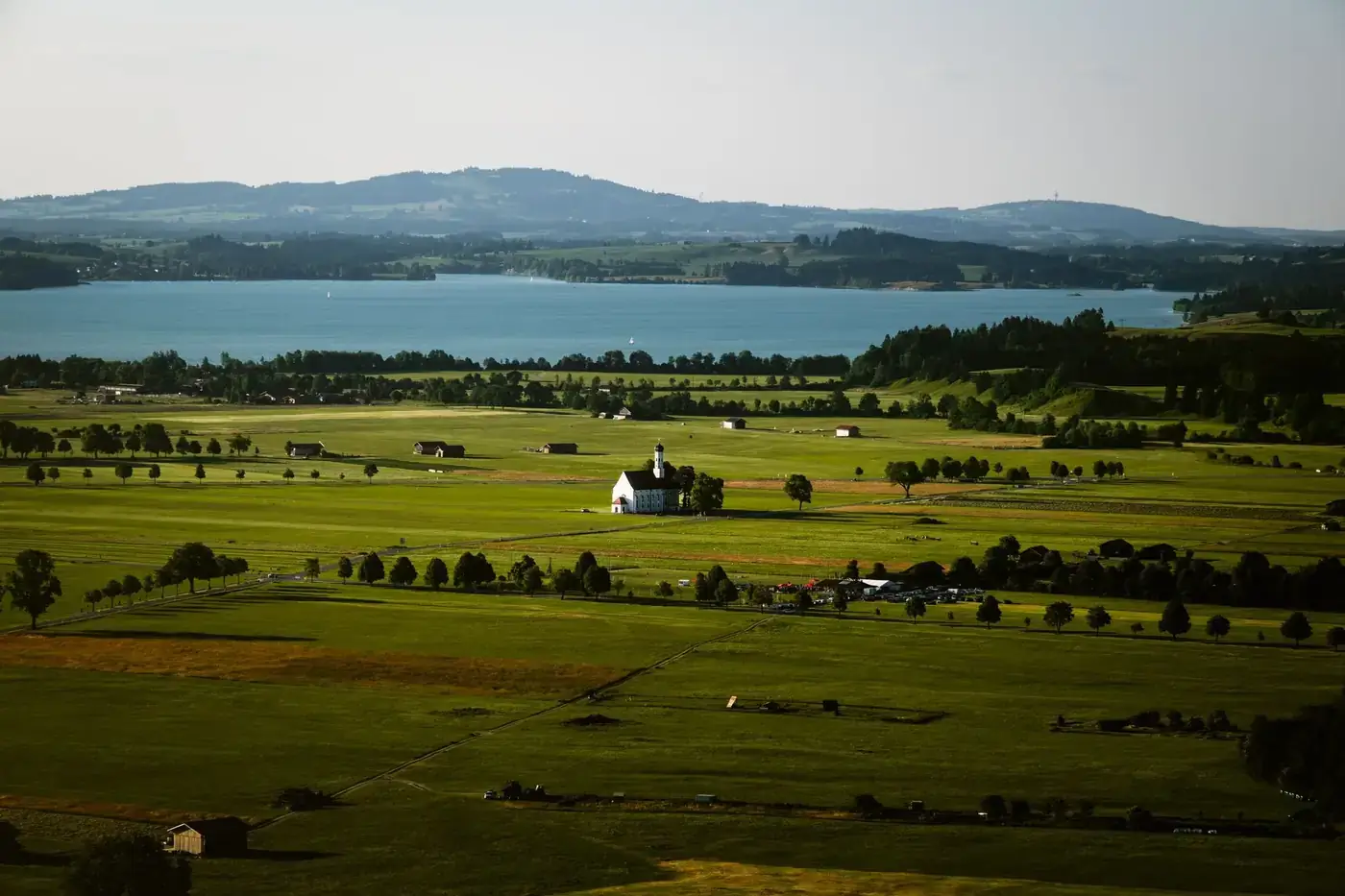 A beautiful aerial view of Füssen, Germany, featuring a picturesque church amidst green fields and a tranquil lake.