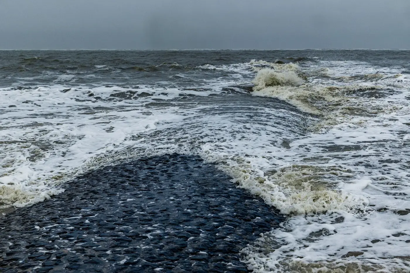 Dynamic view of waves crashing on Baltrum's rocky coast under an overcast sky.