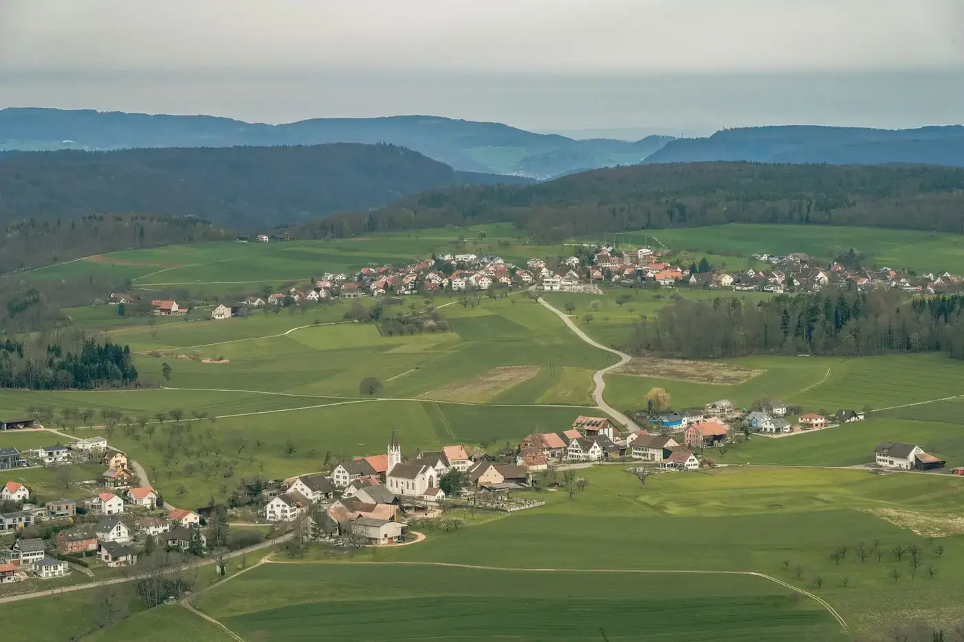 A picturesque aerial view showcasing a serene village surrounded by lush green fields and distant hills.