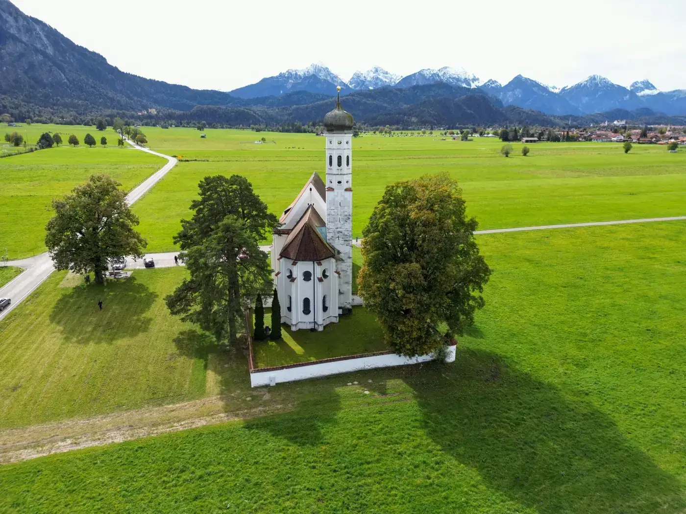 Aerial view of St. Coloman Church surrounded by lush green fields in Schwangau, Germany.