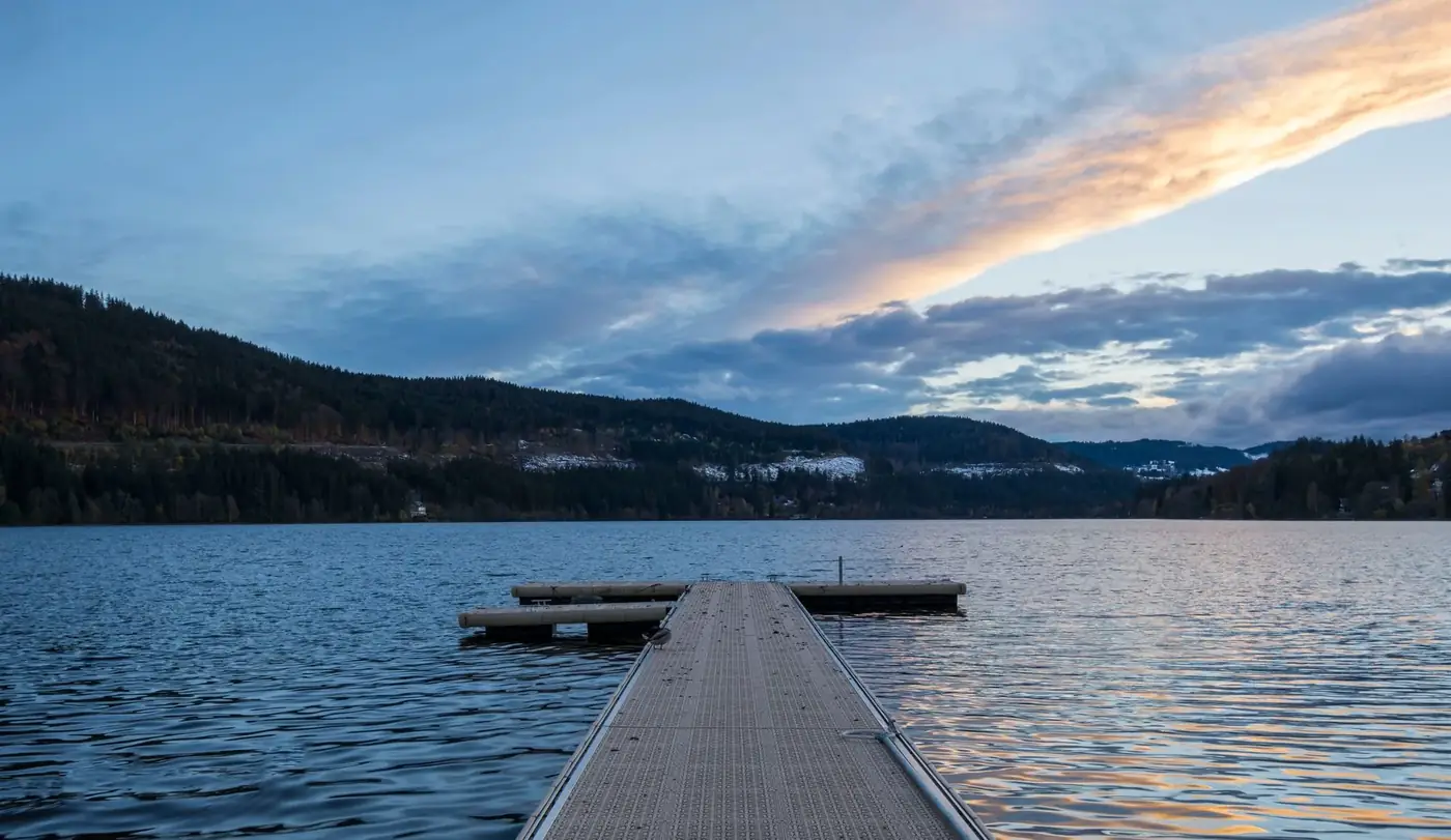 A serene view of dawn breaking over the tranquil Titisee Lake with a dock extending into the calm waters.