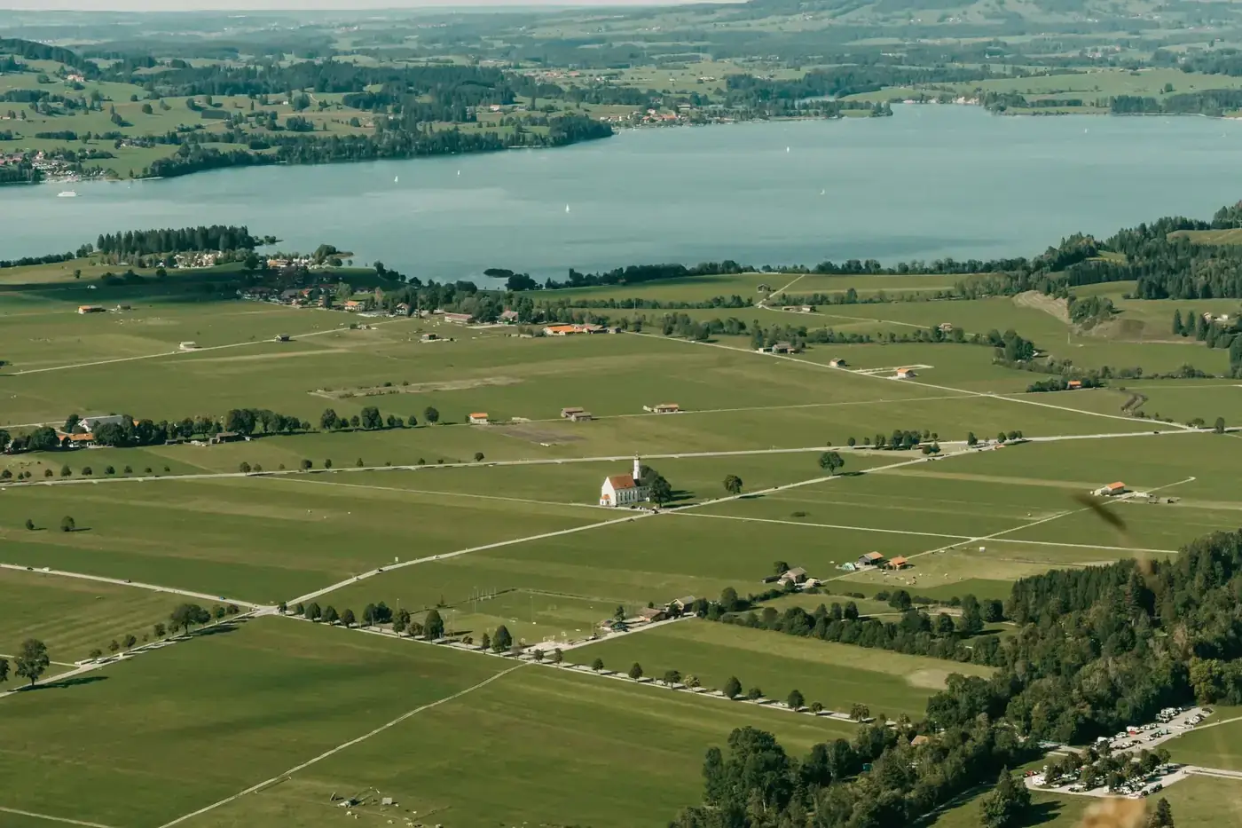 Scenic aerial view of rural Bavaria with fields, church, and lake during summer.