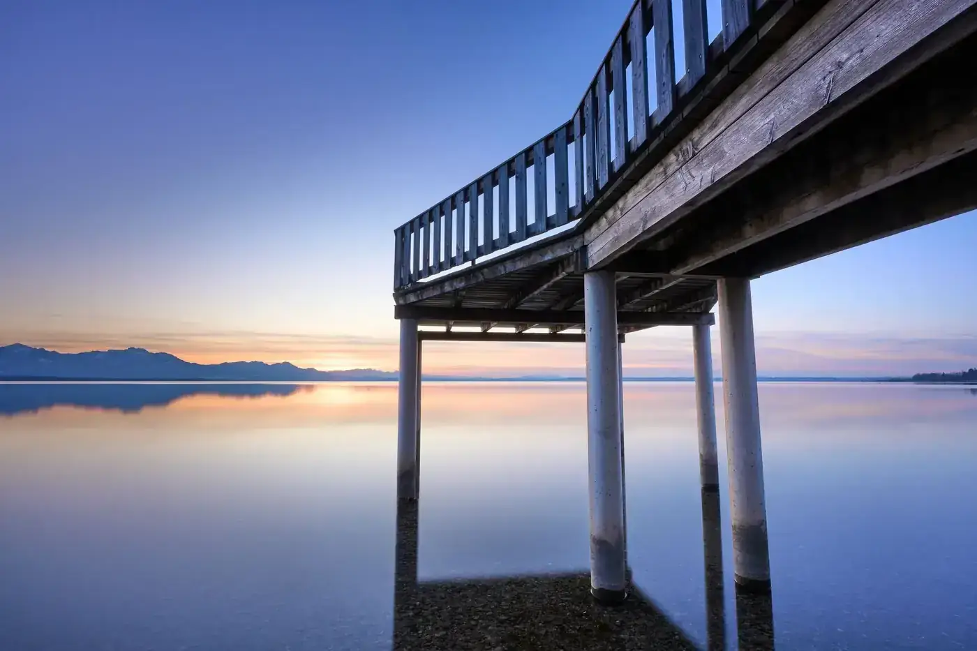 Peaceful wooden pier over calm waters at sunrise in Bayern, Germany.