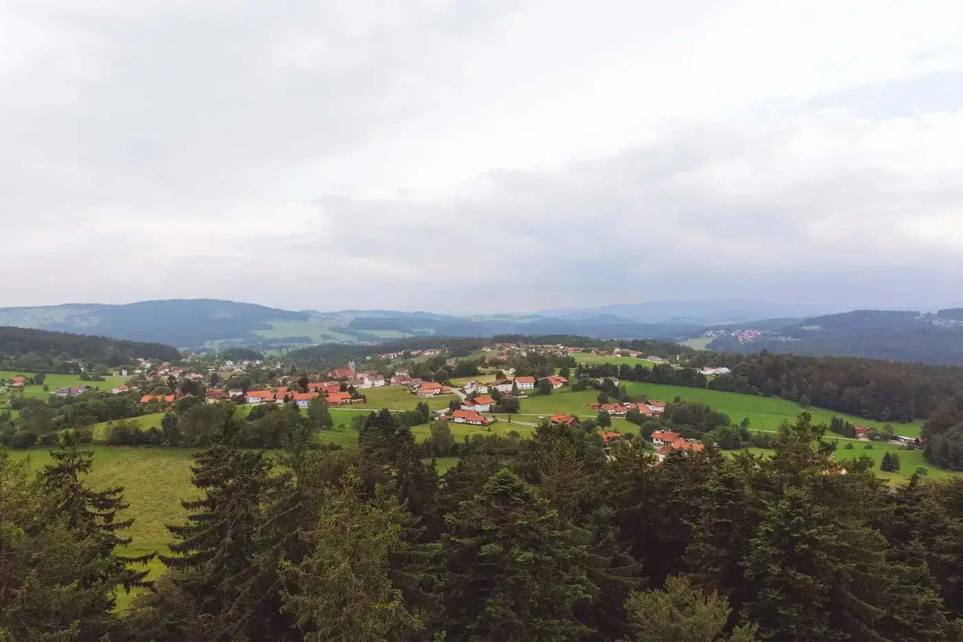 Aerial view of a peaceful Bavarian village surrounded by lush greenery and rolling hills under a cloudy sky.