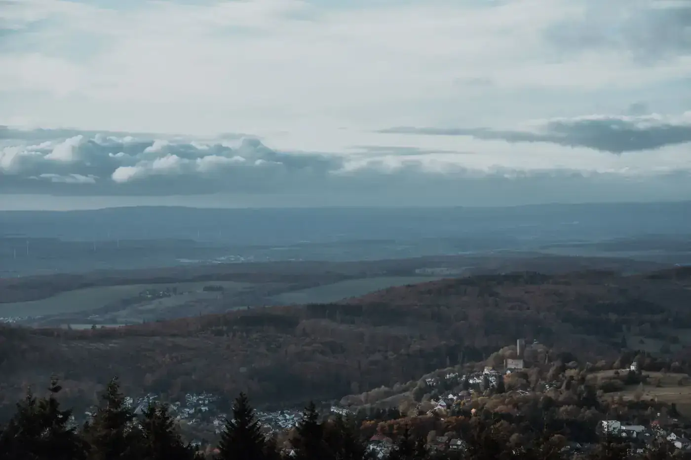Relaxing view of a mountainous landscape in fall, featuring lush forests and a distant village under a cloudy sky.