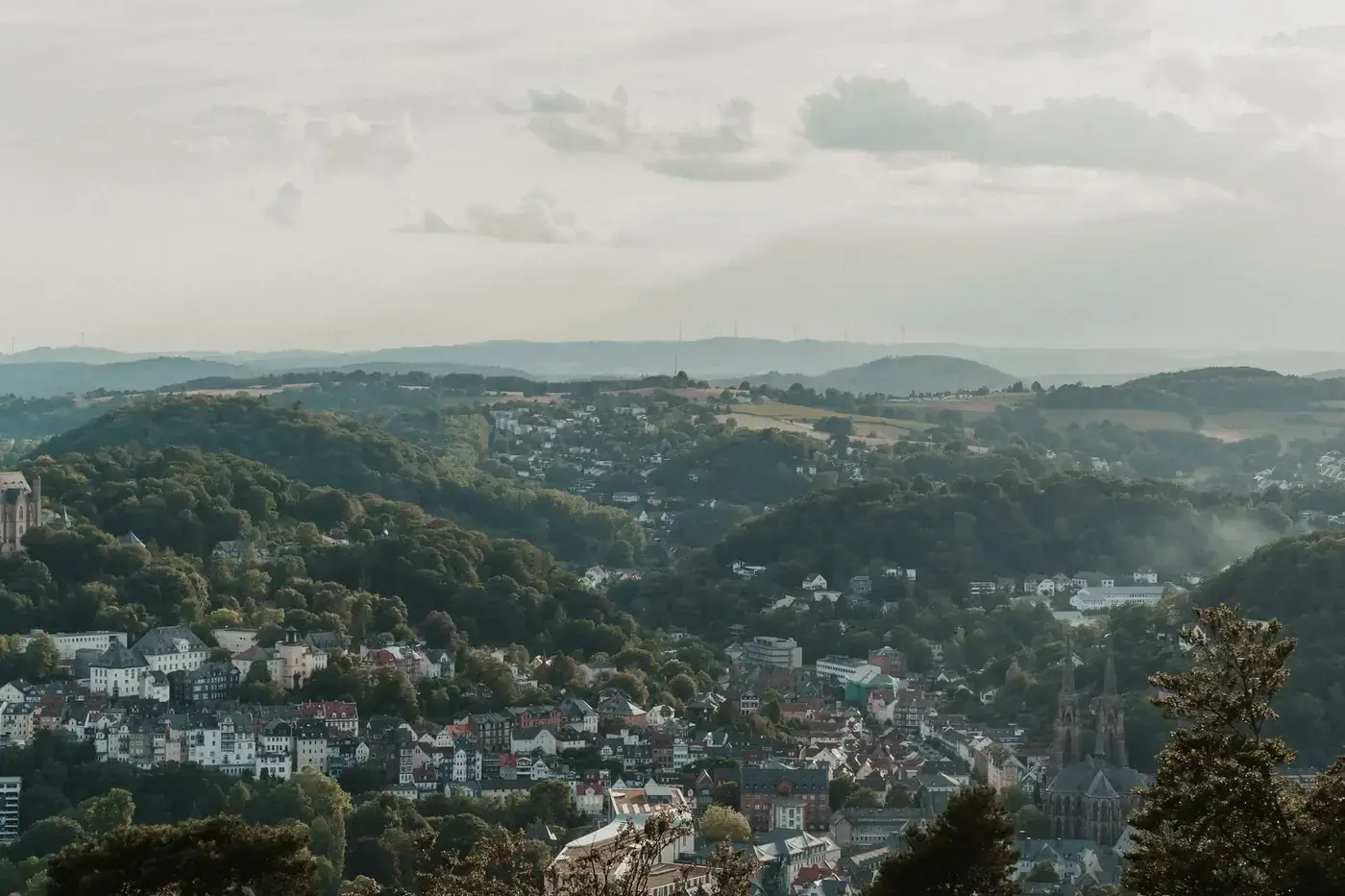 Panoramic view of the town of Eisenach, surrounded by hills and clouds, under muted daylight.