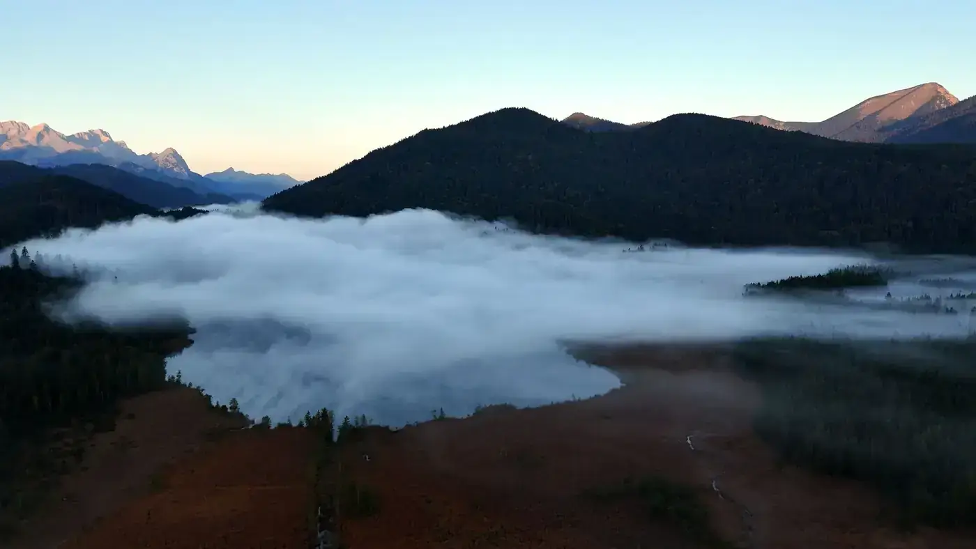 Stunning aerial view of Krün, Bavaria with fog rolling over the valleys at sunrise.