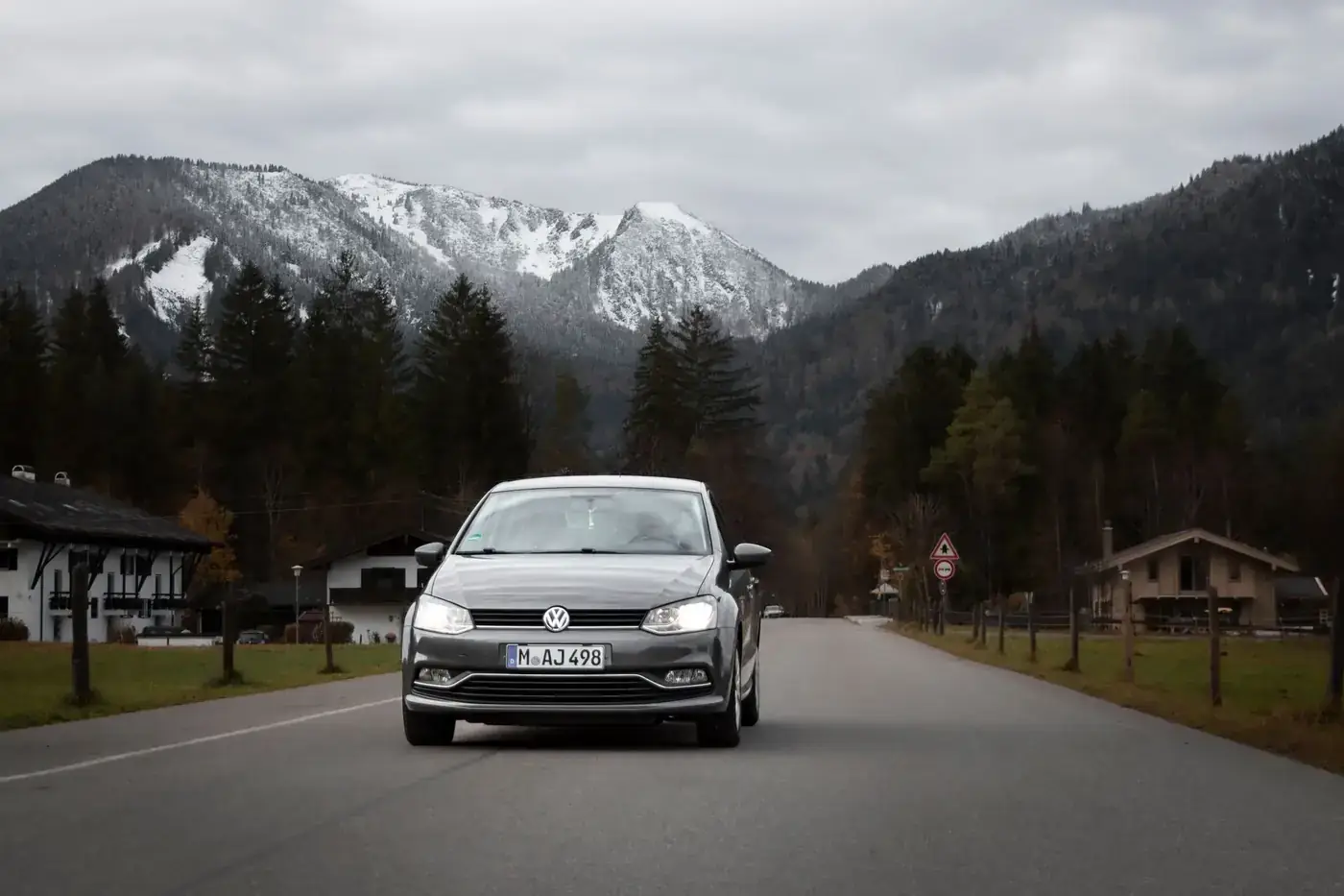 A car travels down a picturesque road near Tegernsee, Germany, with snowy mountains in the background.
