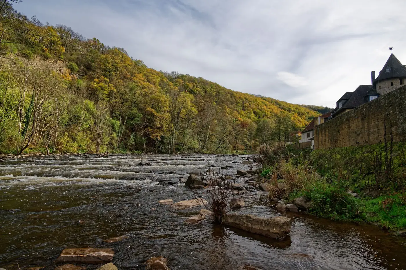 Scenic view of a tranquil river flowing through Meisenheim, surrounded by autumnal forests and a historic village.