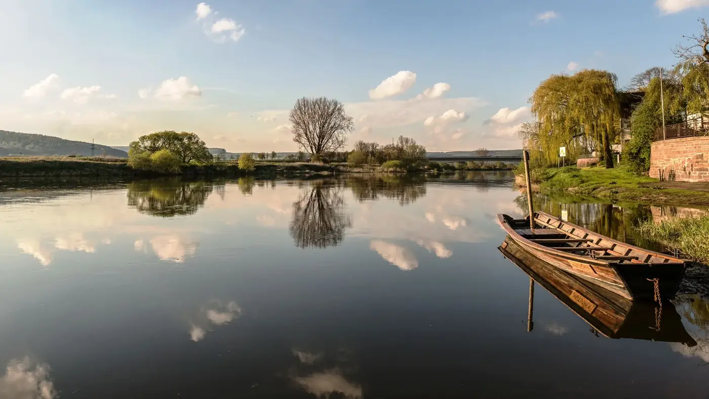 Peaceful river scene with reflections and a wooden boat in Höxter, Germany.
