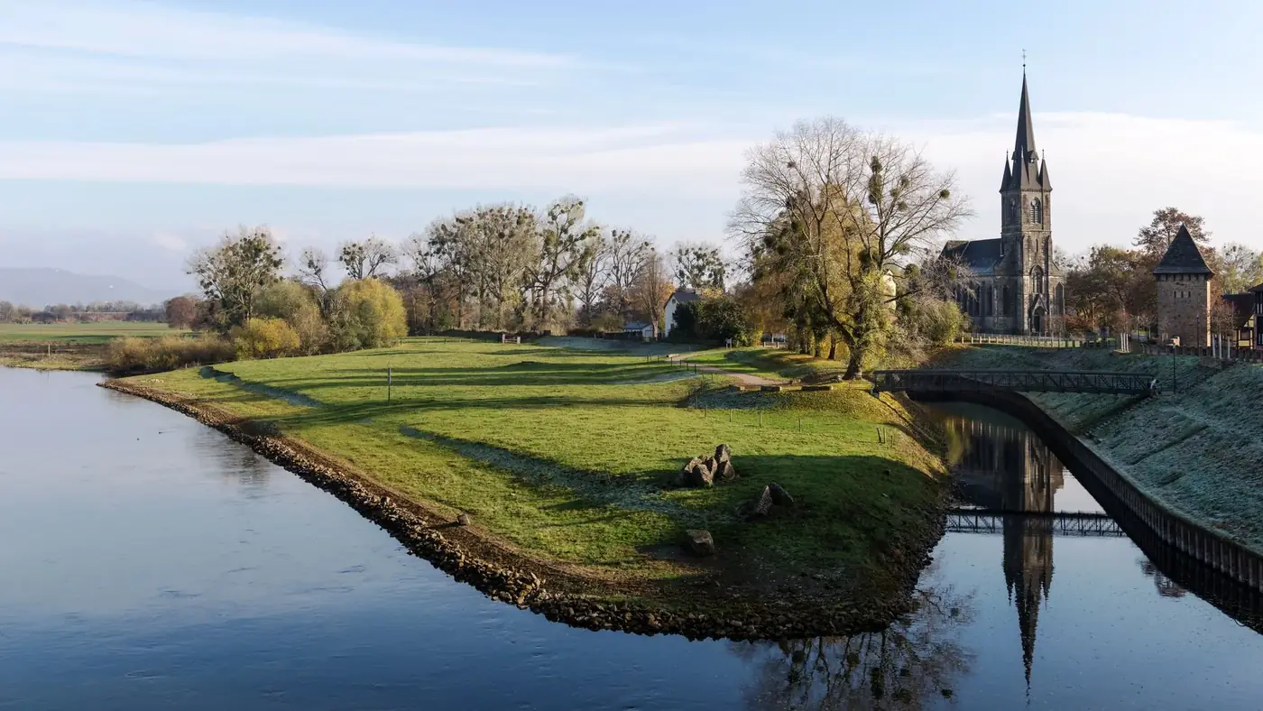 Picturesque autumn landscape of St. Nikolai Church by a tranquil river in Rinteln, Germany.