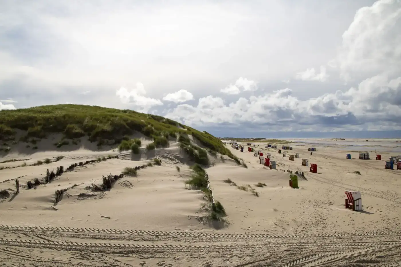A tranquil beach scene featuring dunes and colorful chairs in Wittdün, Germany.