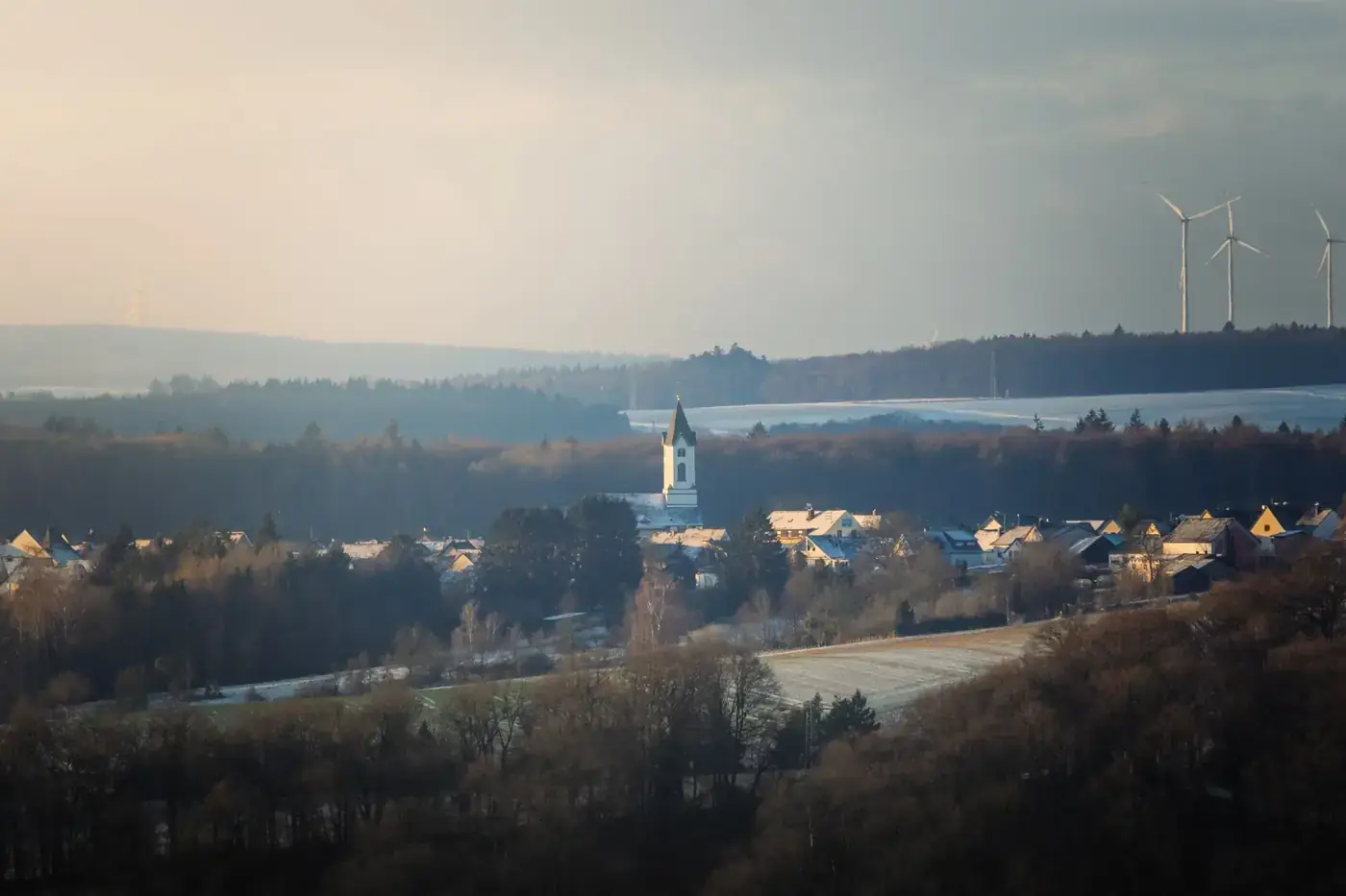 Picturesque village landscape featuring a church and wind turbines during winter twilight.