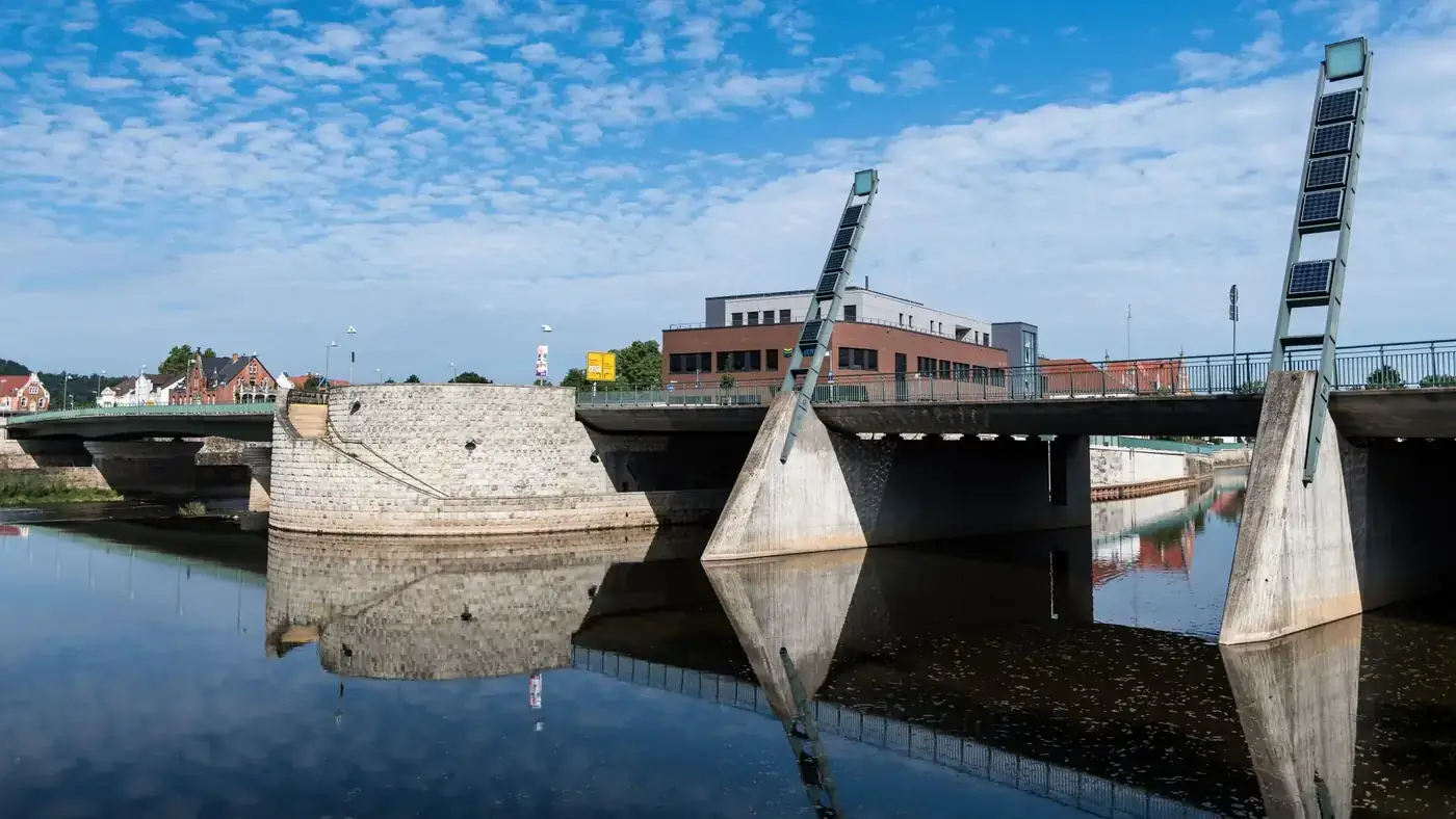 Modern bridge reflecting on Weser River water in Hameln, Germany, under a clear blue sky.